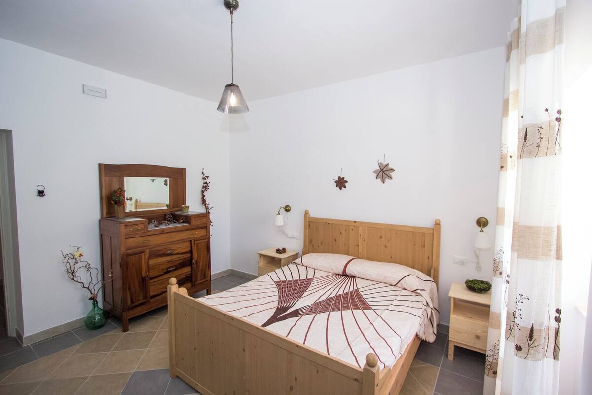 A bedroom with a wooden bed, a dresser, a nightstand, a mirror, and a hanging light fixture.