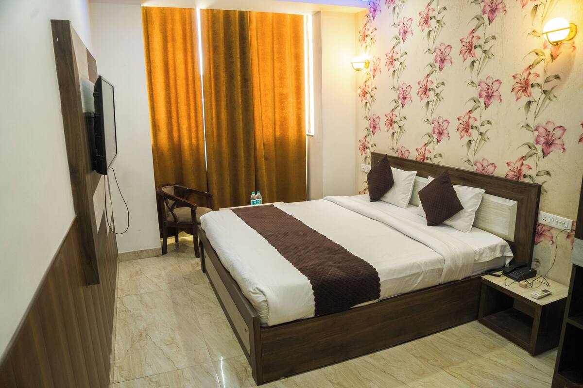 A hotel room with a bed, a chair, a nightstand, a TV, and a floral wallpaper.