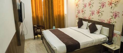 A hotel room with a bed, a chair, a nightstand, a TV, and a floral wallpaper.