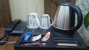 A minibar setup with a kettle, glasses, a phone, and some snacks. - Hotel Amour Chandigarh Zirakpur (Zirakpur)