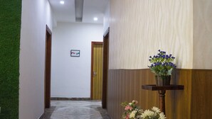 A hallway with a marble floor, wooden paneling, a green wall, and a floral arrangement on a wooden stand. - Hotel Amour Chandigarh Zirakpur (Zirakpur)