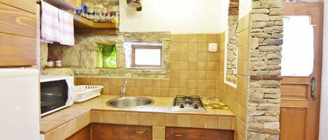 A kitchen with a stone wall, a window, a sink, a stove, and wooden cabinets.