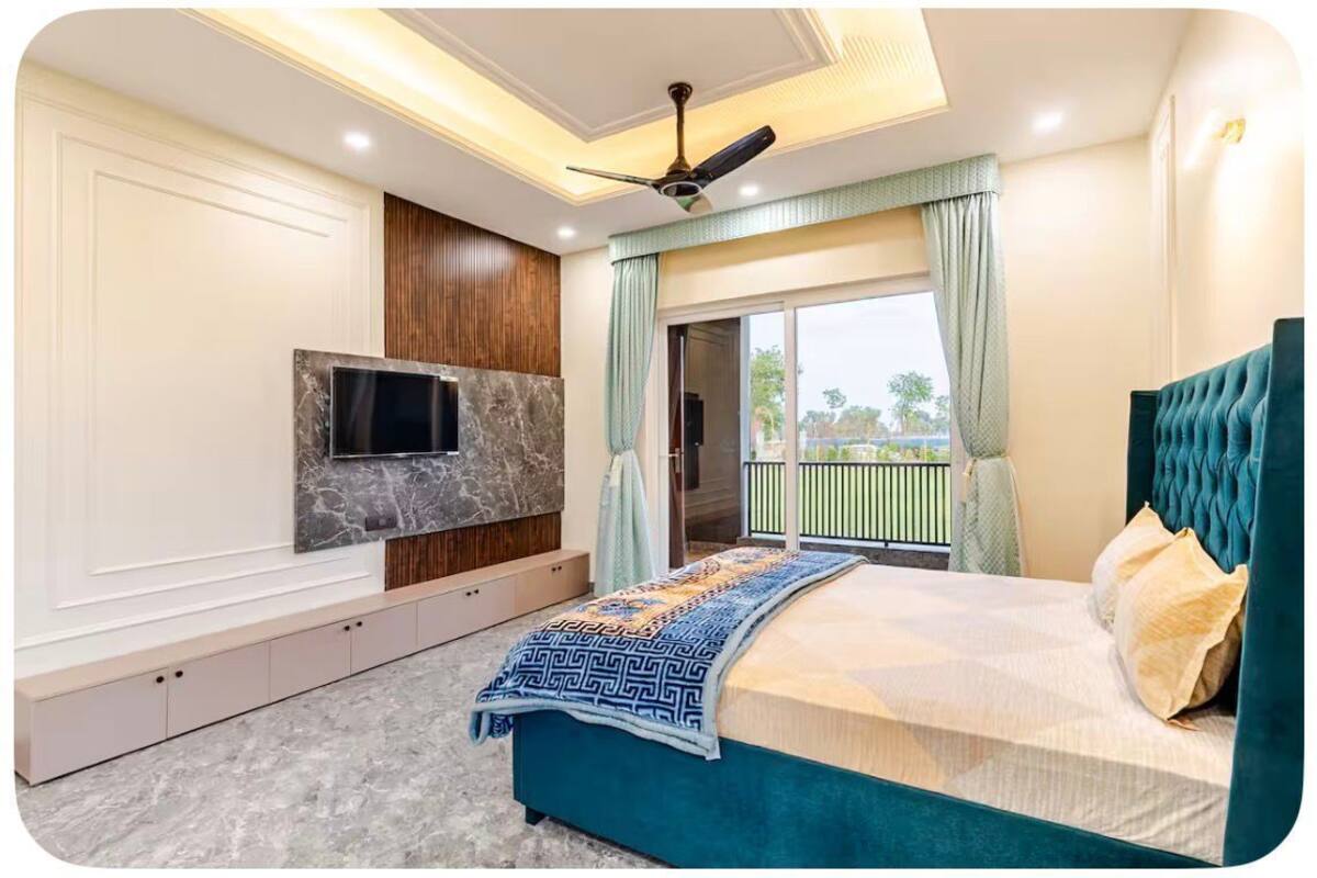A bedroom with a bed, a TV mounted on the wall, a ceiling fan, and a balcony with a view.