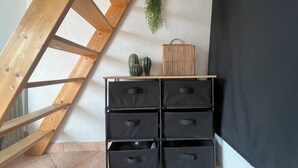 Eine Ecke mit einer Holzleiter, einem schwarzen Stauraum mit Schubladen und einer kleinen Ablage mit Dekoration.