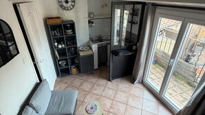 Ein kompakter Wohnbereich mit einer Couch, einem kleinen runden Tisch, einer Küchenzeile mit Spüle und Regalen sowie Blick durch eine Schiebetür.