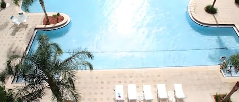 Una gran piscina curvada rodeada de palmeras y sillas de descanso.