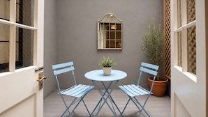 A small patio with a round table and two chairs, a potted plant, and a window with a lattice design. - Luxury Central London Apartment  Craven Street (London)