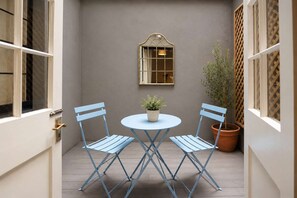 Un pequeño patio con una mesa redonda y dos sillas, una planta en maceta y una ventana con un diseño de celosía.