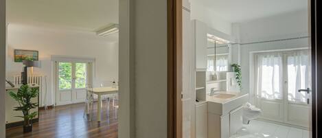 A modern kitchen with white cabinets, a dining area with a white table and chairs, and a bathroom with a white sink and toilet.