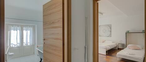 A room with a wooden door, a white sink, a window with curtains, a bed, and a wall-mounted artwork.
