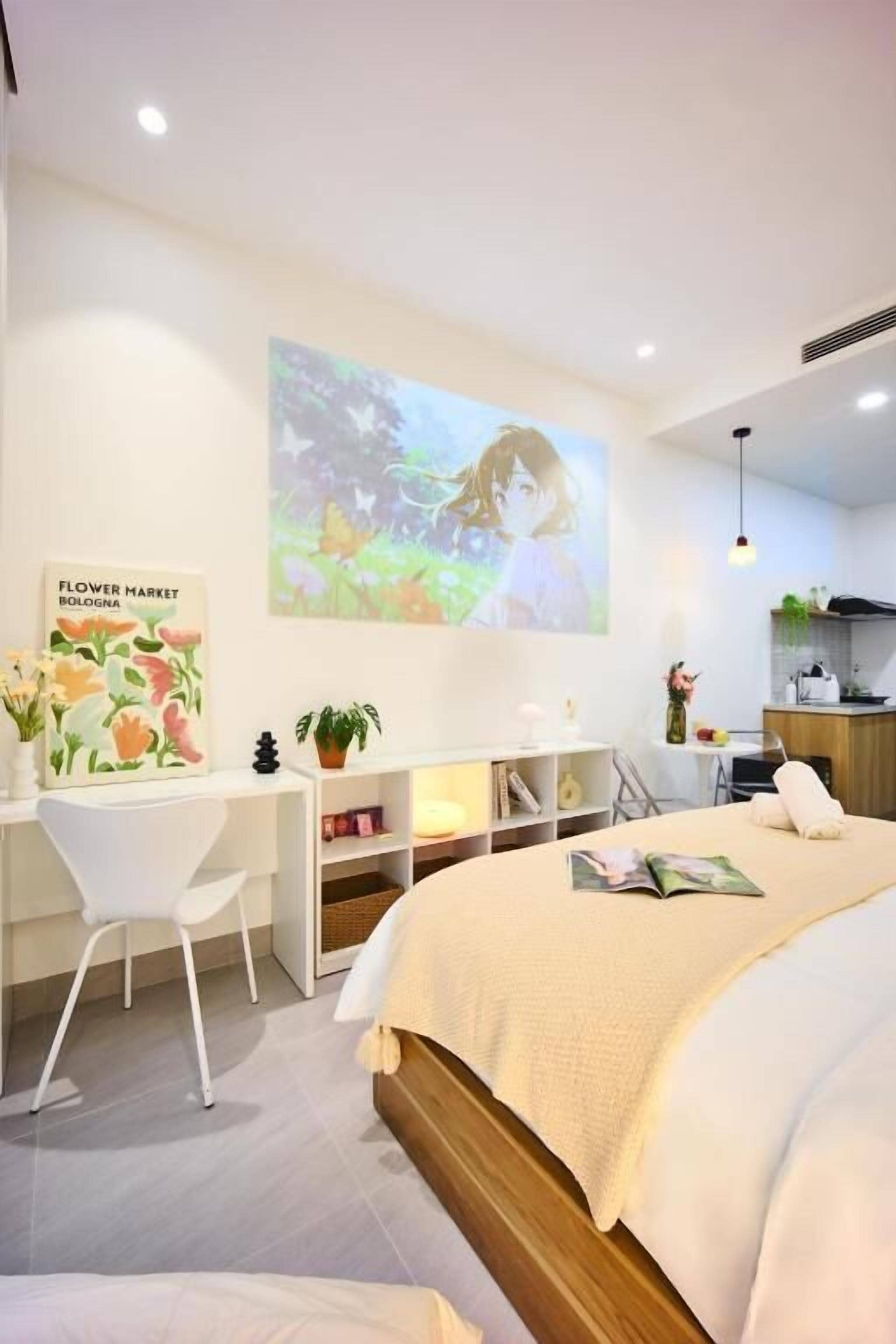 A modern bedroom with a bed, a desk, a chair, a TV, and a kitchen area.