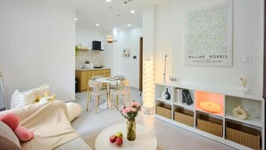 Un salon moderne avec un canapé, une table basse agrémentée de pommes et de fleurs, un coin repas avec des chaises, et une cuisine en arrière-plan.