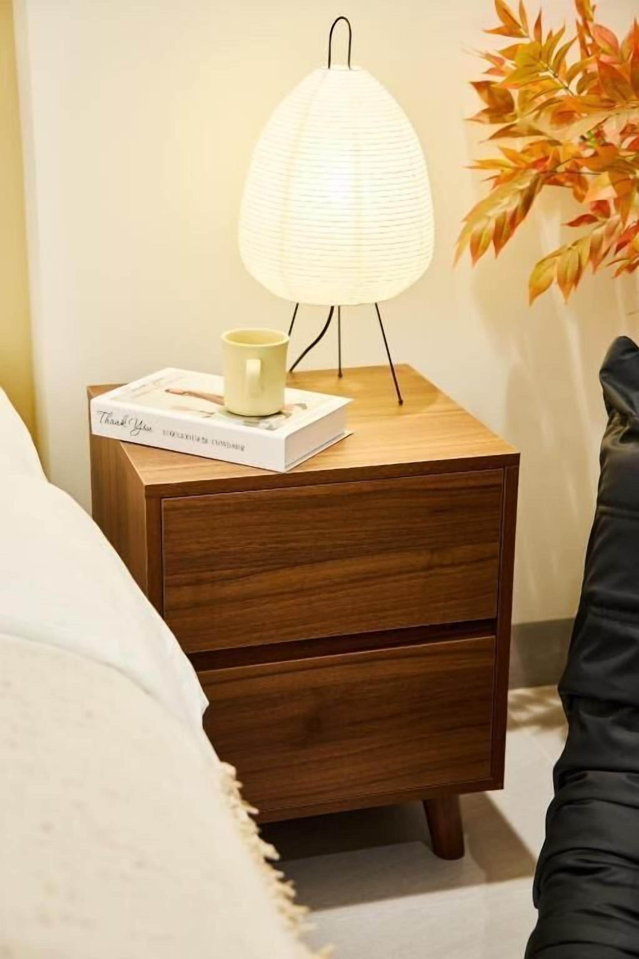 A wooden bedside table with a lamp, a book, and a mug.
