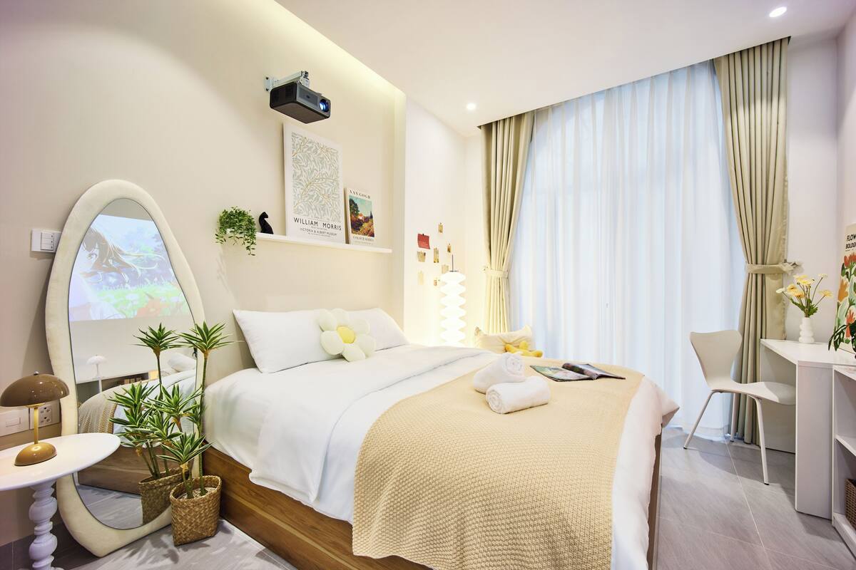 Una habitación de hotel con cama, mesita de noche, lámpara, plantas en macetas, escritorio y un espejo grande.