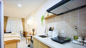 Une chambre d’hôtel de taille réduite, équipée d’une kitchenette, d’un lit, d’un bureau et d’une chaise.