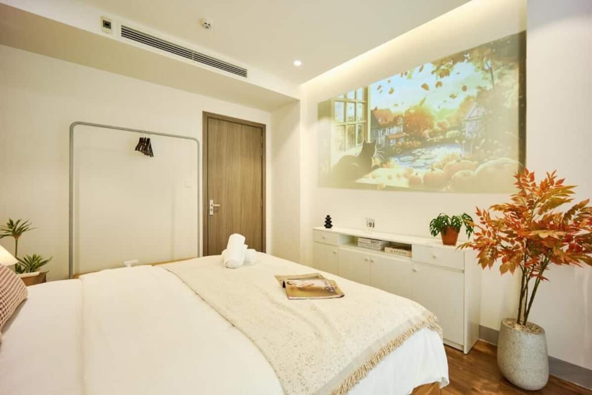 Un dormitorio con una cama, una mesita de noche, una pantalla de televisión, una puerta y una planta en maceta.