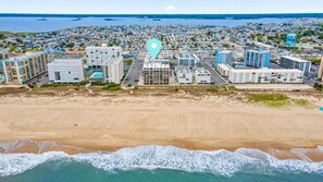 Vista aérea de uma cidade costeira com um complexo hoteleiro na orla, incluindo vários edifícios, uma praia de areia e o oceano.