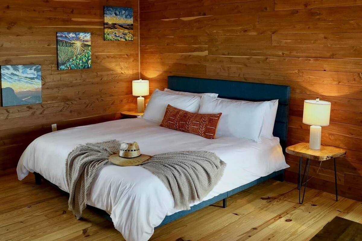 A wooden-paneled room with a bed, two bedside lamps, and wall art.