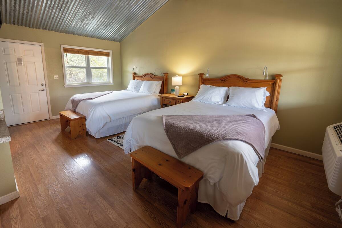 A room with two beds, a wooden bench, a window, and a door.