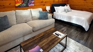 Una habitación acogedora con techo de madera, una cama, un sofá, una mesa de centro y un cuadro en la pared.