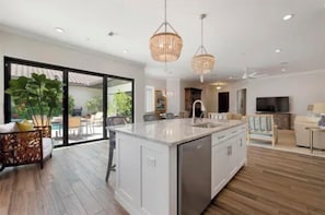 Een moderne keuken met een groot eiland, hanglampen en een schuifdeur naar een buitenruimte.
