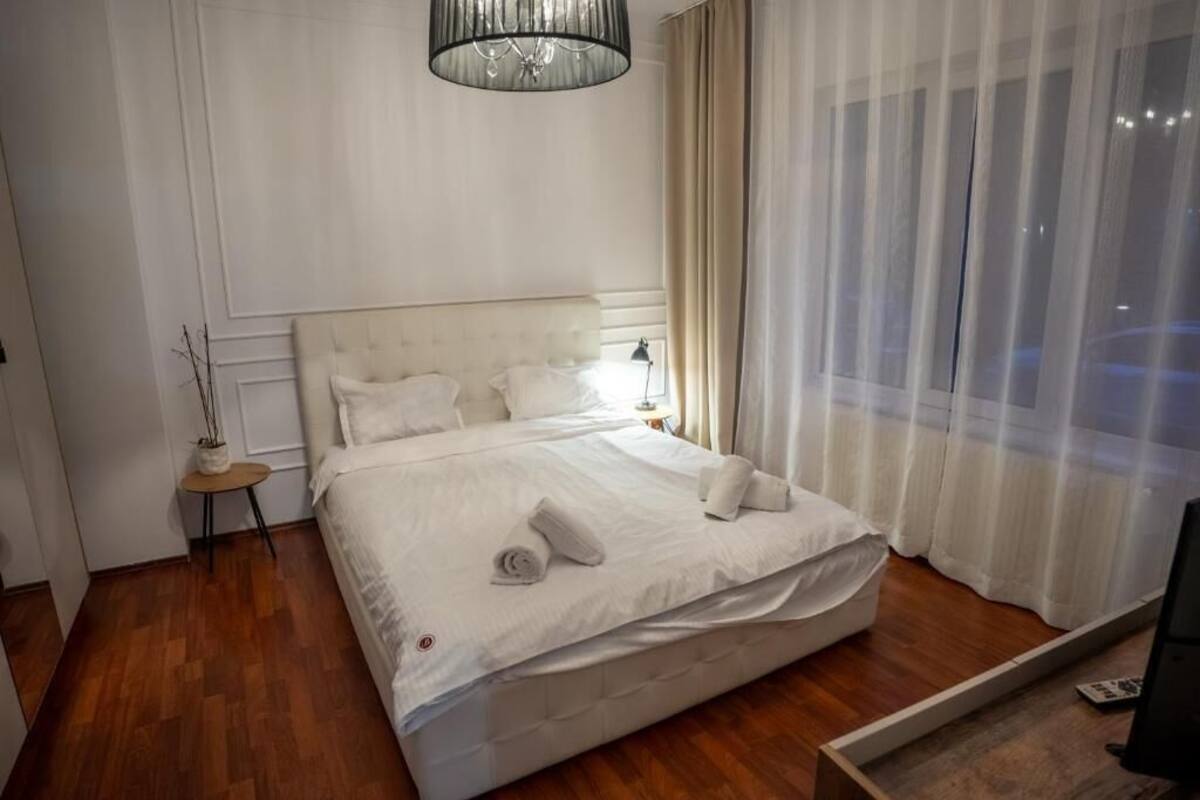 Habitación de hotel con una cama grande, una mesita de noche, una lámpara y una ventana con cortinas translúcidas.