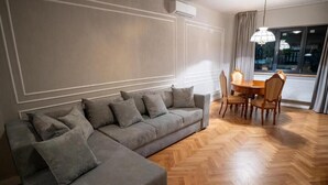 A modern living room with a grey sectional sofa, a wooden dining table with chairs, and a large window with curtains. - Barrique Eminescu 14 (Brașov)