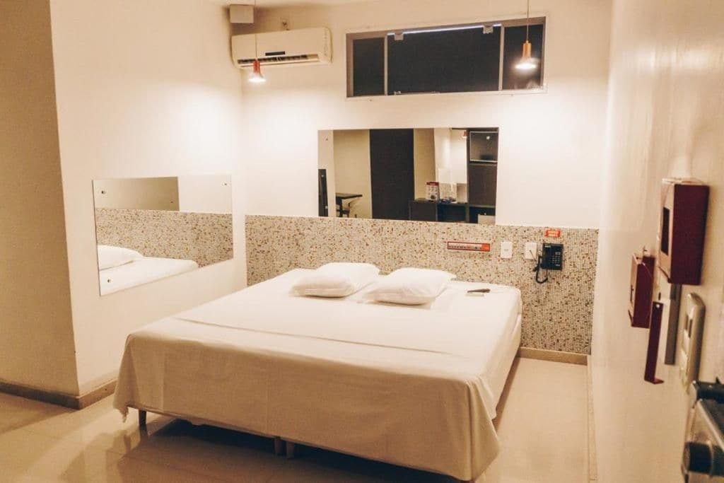 Una habitación de hotel con cama, espejo, teléfono y aire acondicionado instalado en la pared.