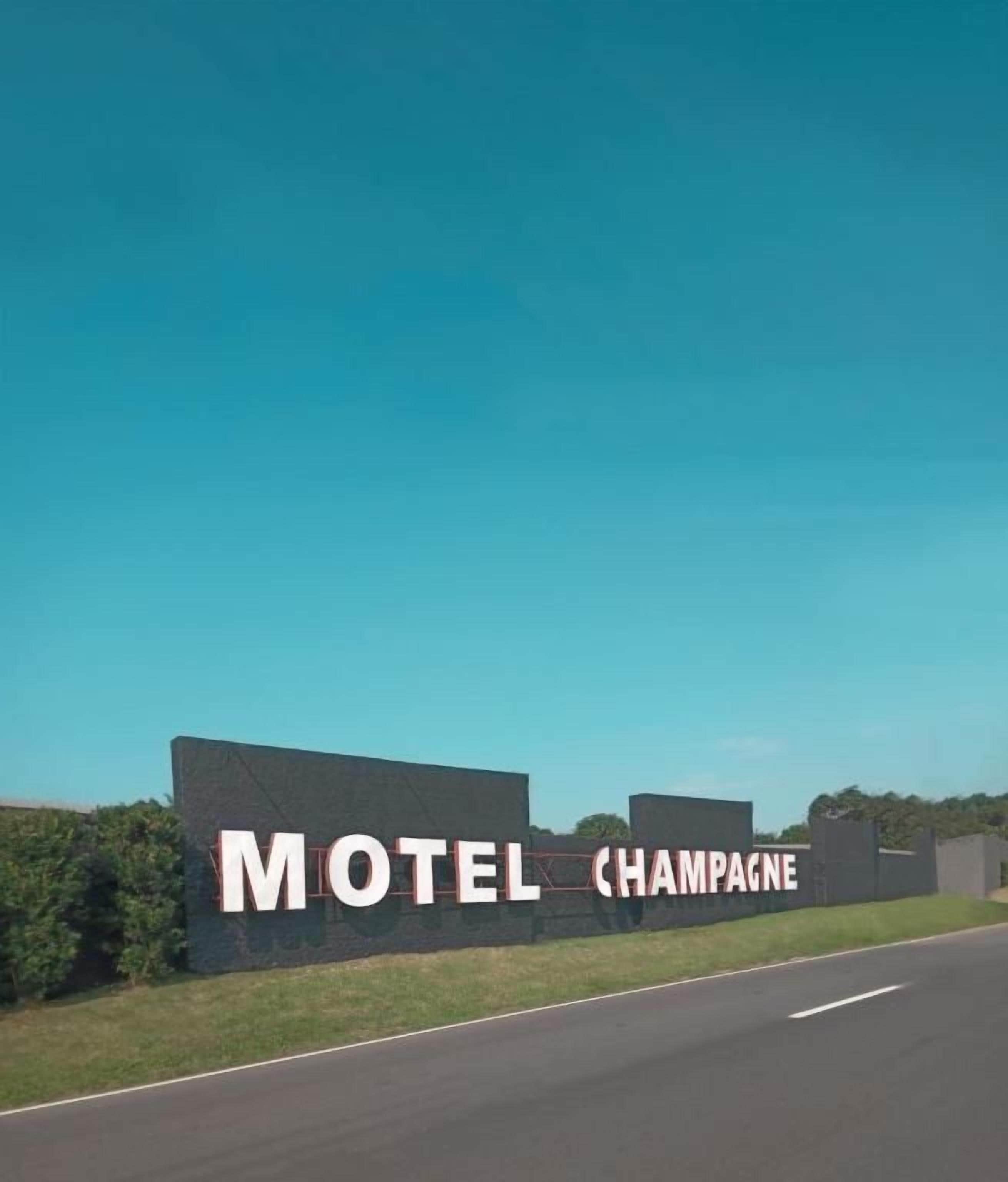 Señal de motel con el nombre 'Motel Champagne' en un día despejado.