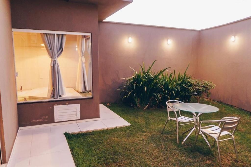 A small patio area with a glass table and chairs, a window with curtains, and a potted plant.