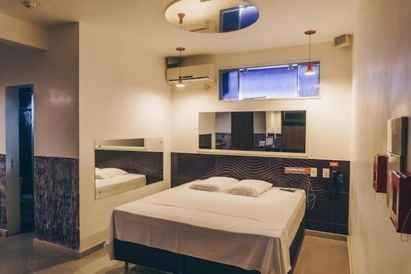 Una habitación de hotel con cama, espejo, ventana y aire acondicionado de pared.