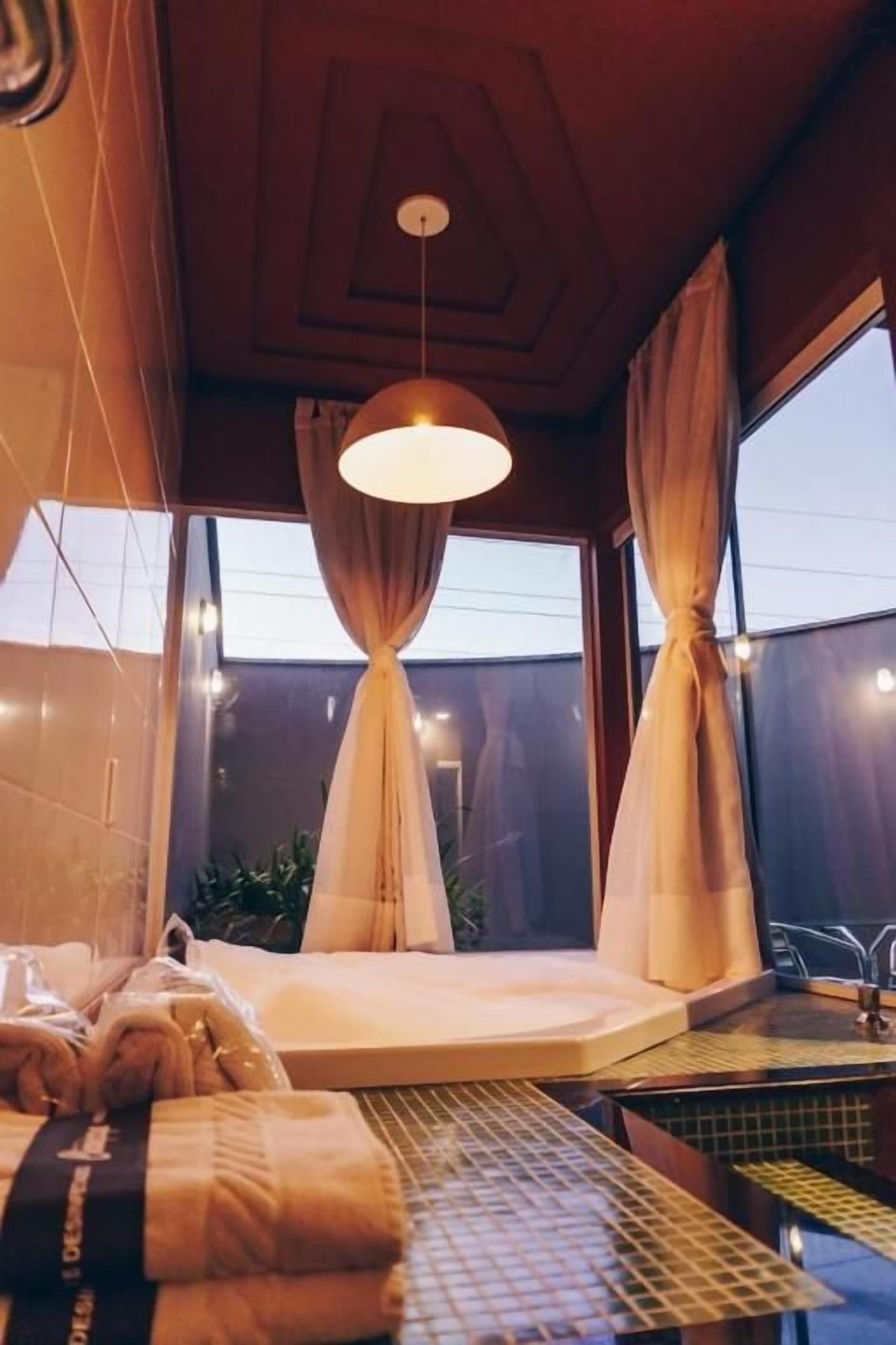 A room with a bed, a window with curtains, a hanging light fixture, and a small table with a tray.