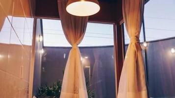 A room with a bed, a window with curtains, a hanging light fixture, and a small table with a tray.