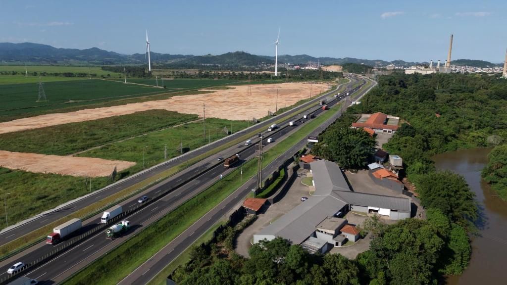 A highway with multiple lanes, a river, and industrial structures in the background.