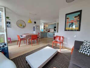 A modern living room with a sofa, a dining table with chairs, a kitchen in the background, and a large window. - Perros-Guirec - charming 4-person apartment - garden/terrace, walking distance to beach (Perros-Guirec)