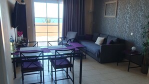 Un salon comprenant un canapé, une table à manger avec des chaises, un ventilateur de plafond et une vue sur l’extérieur.
