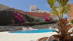 Un espace piscine avec des chaises longues, un mur en pierre et un bâtiment doté de balcons en arrière-plan.