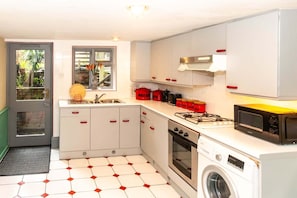 A compact kitchen with a washing machine, a microwave, and a gas stove. - Stylish early Victorian garden apartment located near centre of London UK (London)