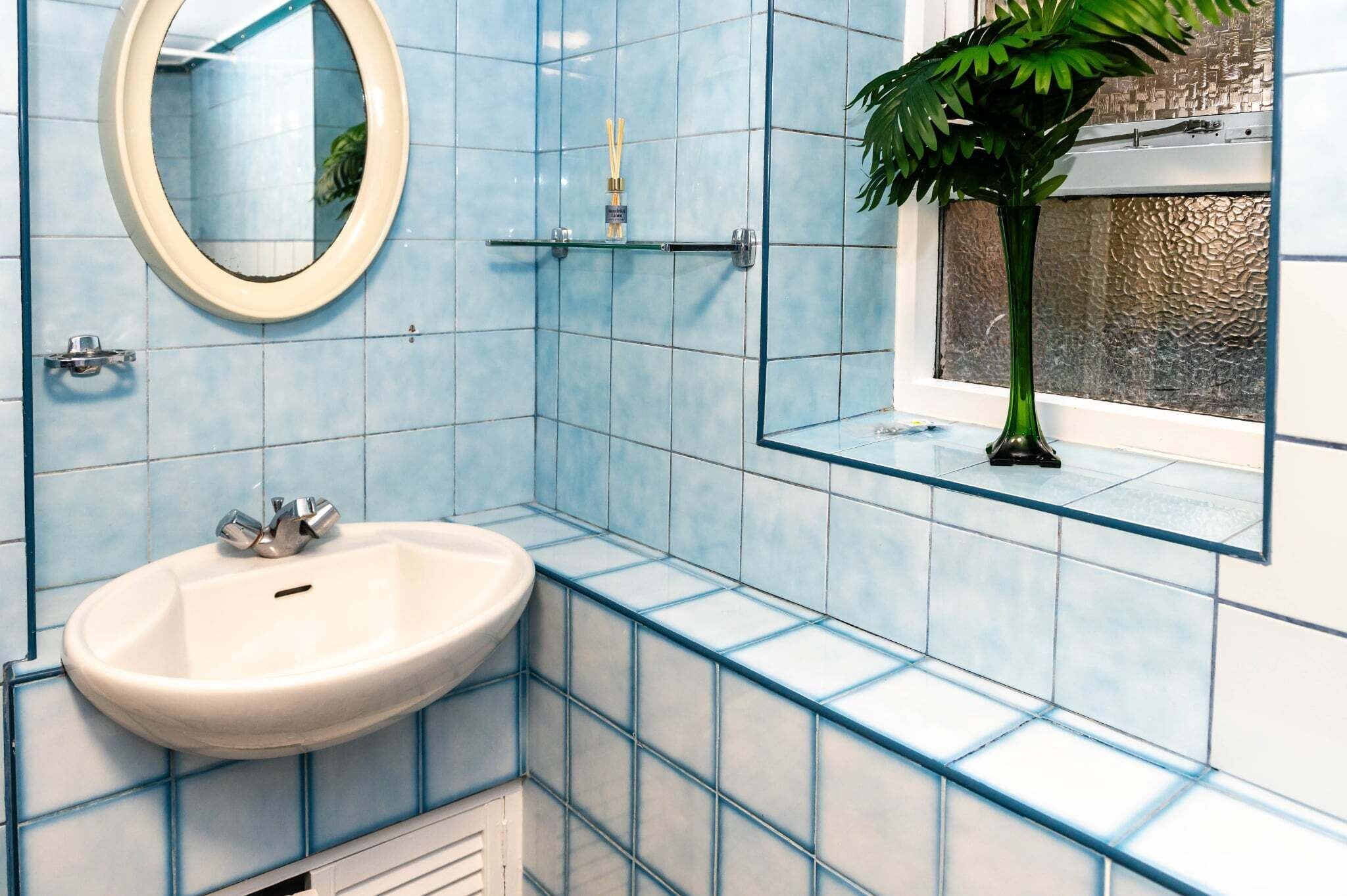 A bathroom with a white sink, a mirror, and a window with a plant.