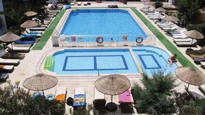 Ein Pool mit Liegestühlen und Sonnenschirmen, umgeben von Grünflächen.