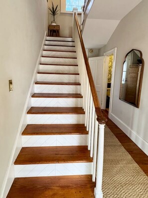 Una escalera de madera con barandillas blancas que lleva a una habitación con un espejo grande y una puerta.