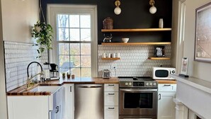 A modern kitchen with white cabinetry, a wooden countertop, stainless steel appliances, and a black backsplash. - Historic DT Lynchburg Apt, Walk To Shops & Dining (Lynchburg)