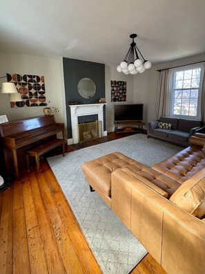 Una sala de estar con chimenea, sofá, televisor y piano.