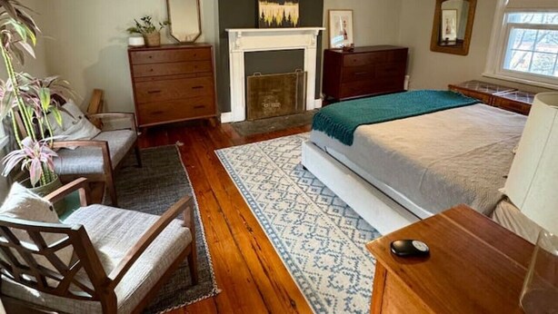 A bedroom with a bed, a dresser, a chair, a desk, a fireplace, and a ceiling fan. - Historic DT Lynchburg Apt, Walk To Shops & Dining (Lynchburg)