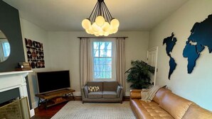 A living room with a sofa, a television, a fireplace, and a world map on the wall. - Historic DT Lynchburg Apt, Walk To Shops & Dining (Lynchburg)