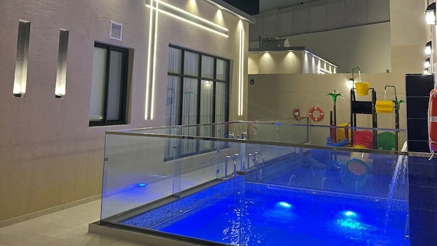 Una piscina con barrera de vidrio, suelo de baldosas y un edificio con líneas iluminadas en la pared.