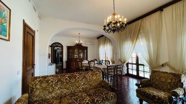 Ein Wohnzimmer mit gestreiften Sofas, einem Chandelier, einem Essbereich mit Tisch und Stühlen sowie einer Küche im Hintergrund.