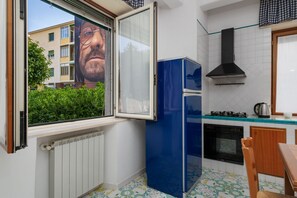 Eine kleine Küche mit Fenster, einem blauen Kühlschrank, einem Herd und einem Fliesenboden.