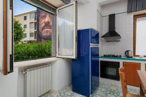 Eine kleine Küche mit Fenster, einem blauen Kühlschrank, einem Herd und einem Fliesenboden.