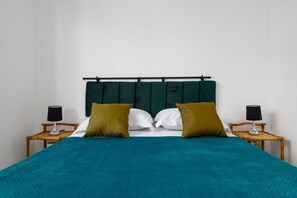 Ein Bett mit türkisfarbener Bettdecke, zwei Kissen, einem dunklen Kopfteil und zwei Nachttischen mit Lampen.